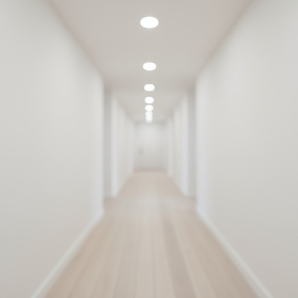 A blurred perspective looks down a clean white hallway featuring light wood flooring and neutral white recessed ceiling lights.
